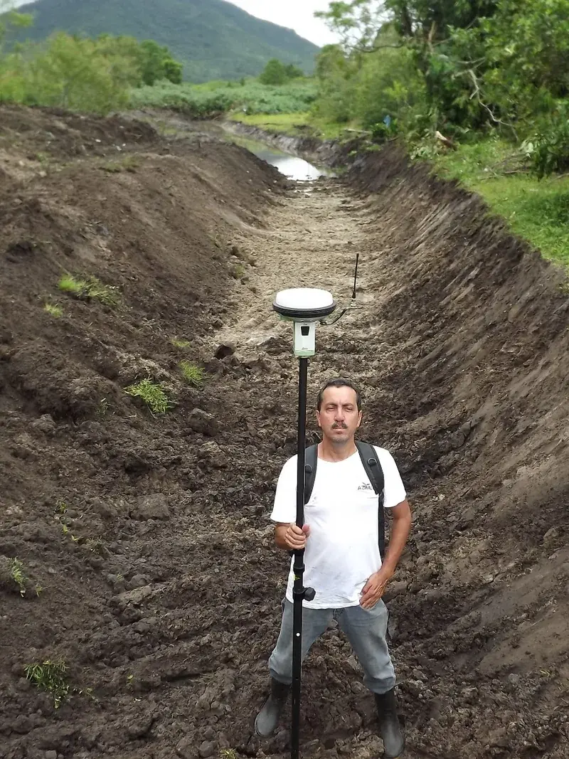 Profissional da EGN com receptor GNSS montado em bastão realizando levantamento topográfico dentro da vala de contenção